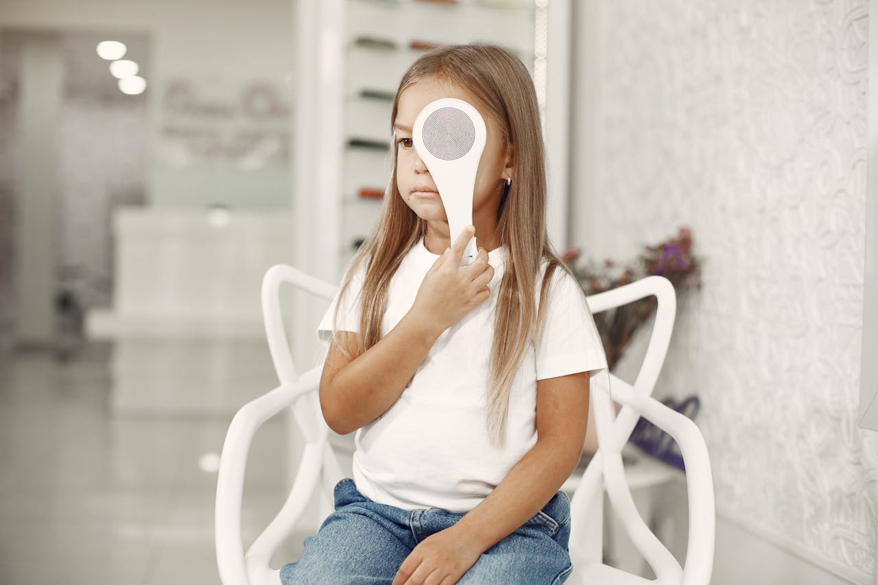 Badanie wzroku A young girl undergoing an eye test at an optician clinic, seated and holding an eye occluder.